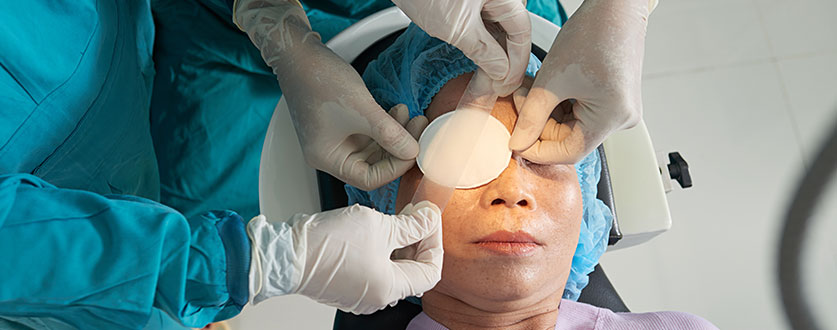 Surgeons in blue scrubs place an eye patch over a patient’s eye.